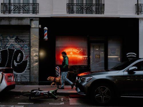 Man walks dog past barbershop with neon sign